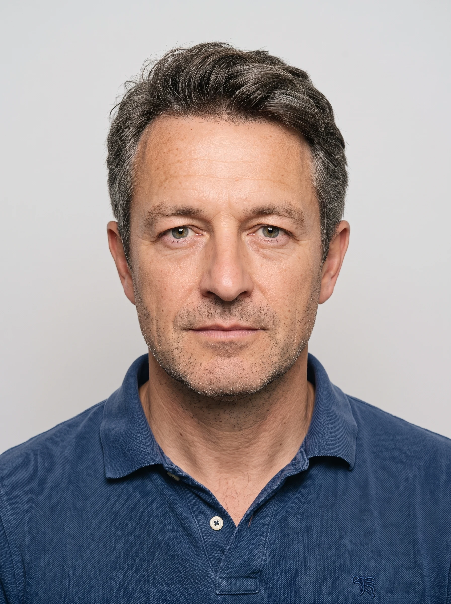 The same man as a UK-standard passport photo: plain grey background, even lighting, neutral expression