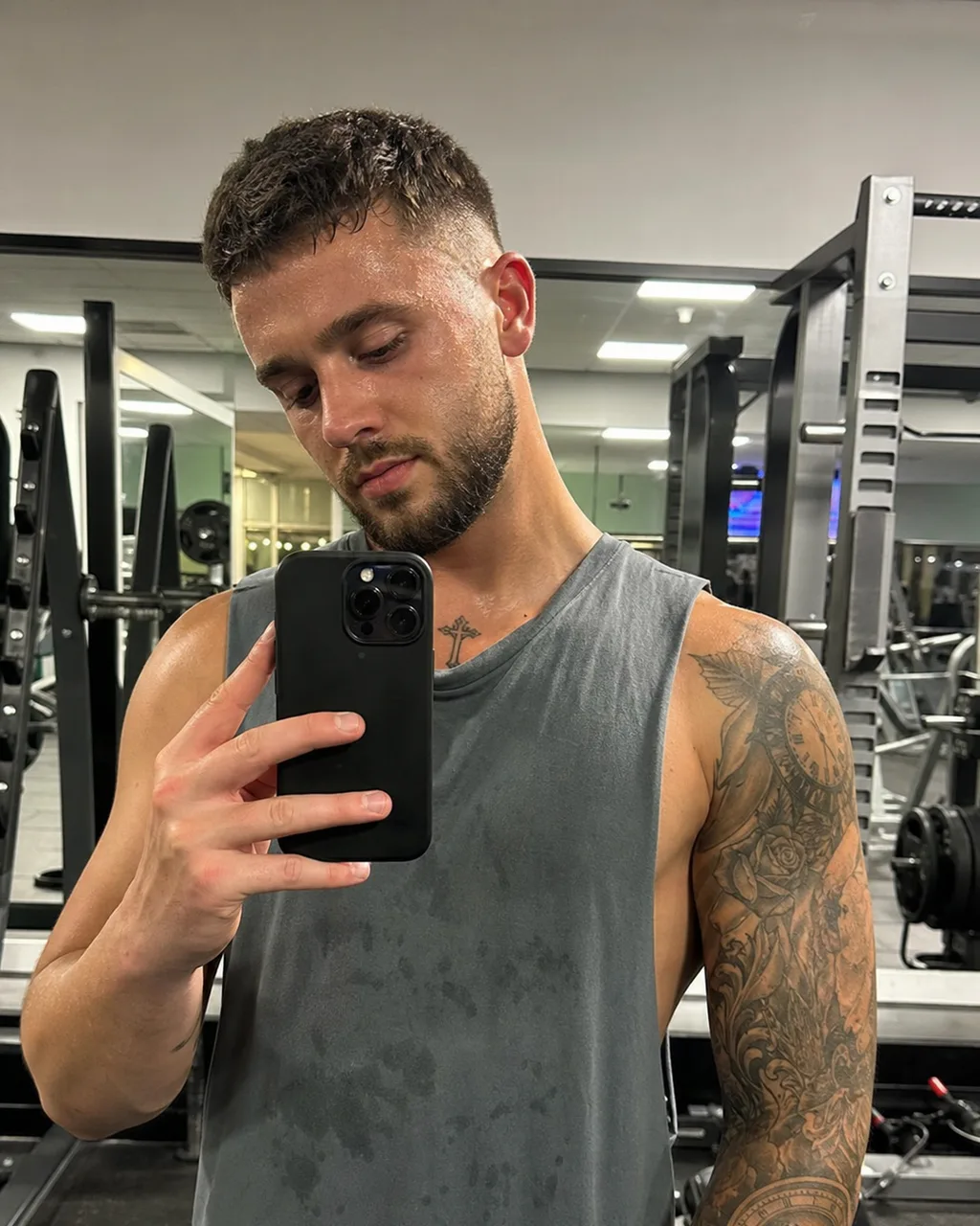Gym mirror selfie under flat fluorescent lighting with racks and mirrors in the background