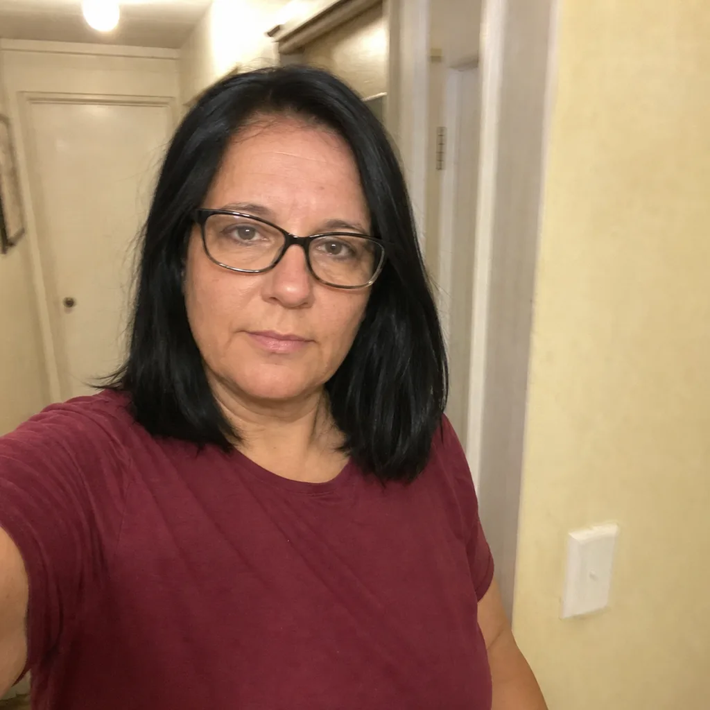 Casual phone selfie of a woman in a t-shirt in a dim hallway