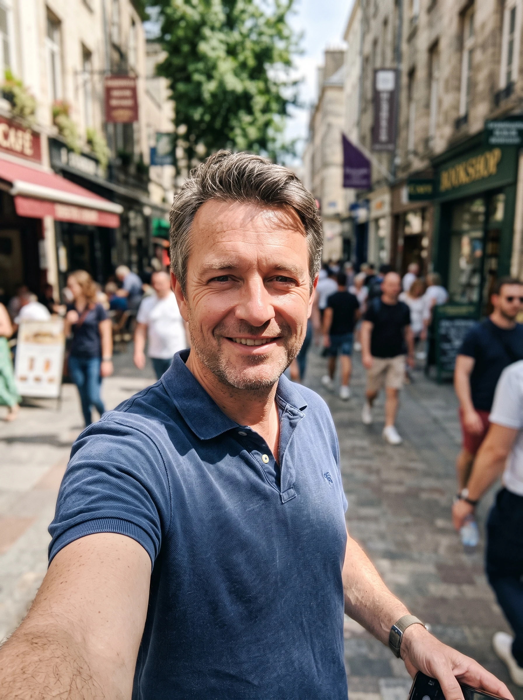 Man taking a smiling selfie on a sunny street with harsh uneven light and a busy background