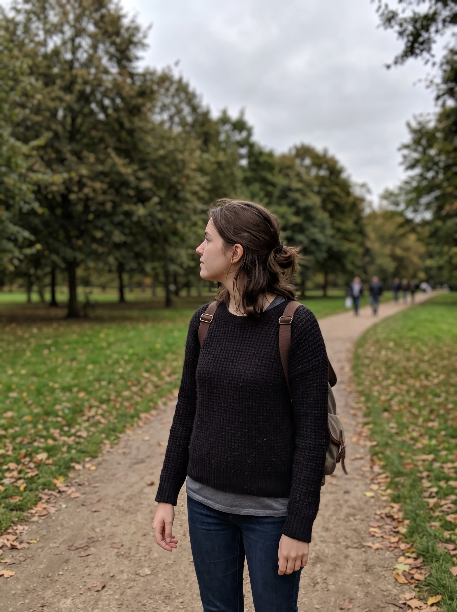 Woman standing on a park path turned away from the camera in three-quarter profile