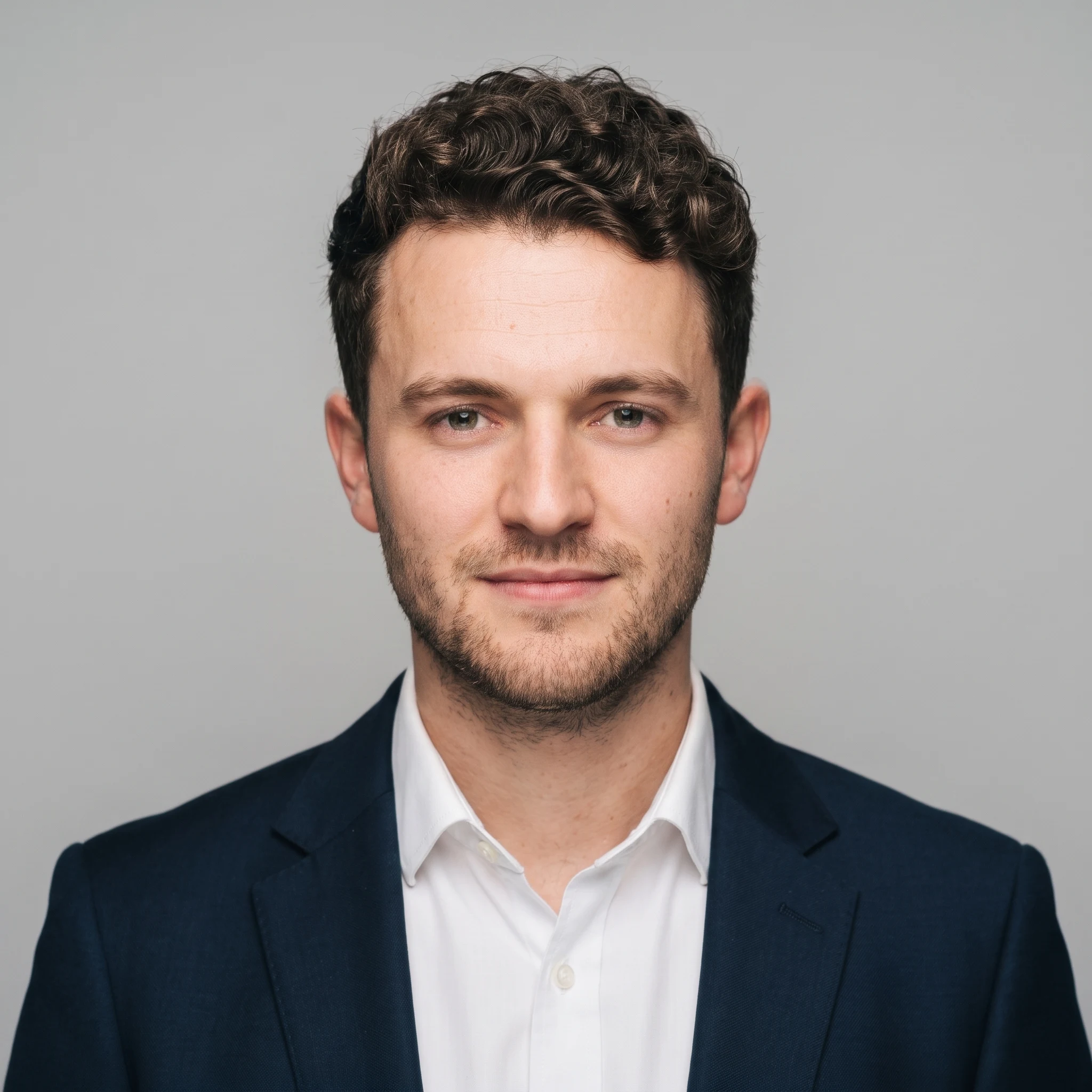 The same man as a studio headshot in a navy suit on a light grey background, strangers removed