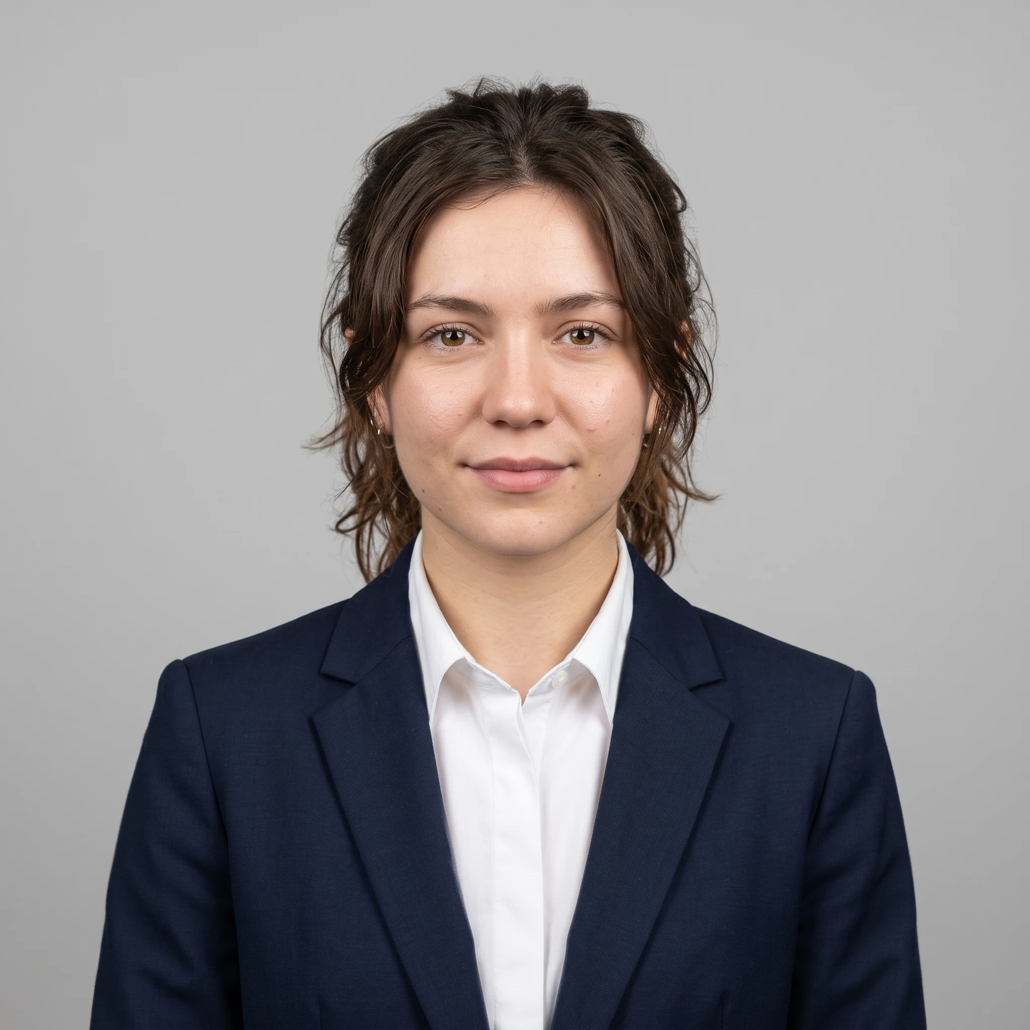 The same woman as a studio headshot in a navy suit on a light grey background